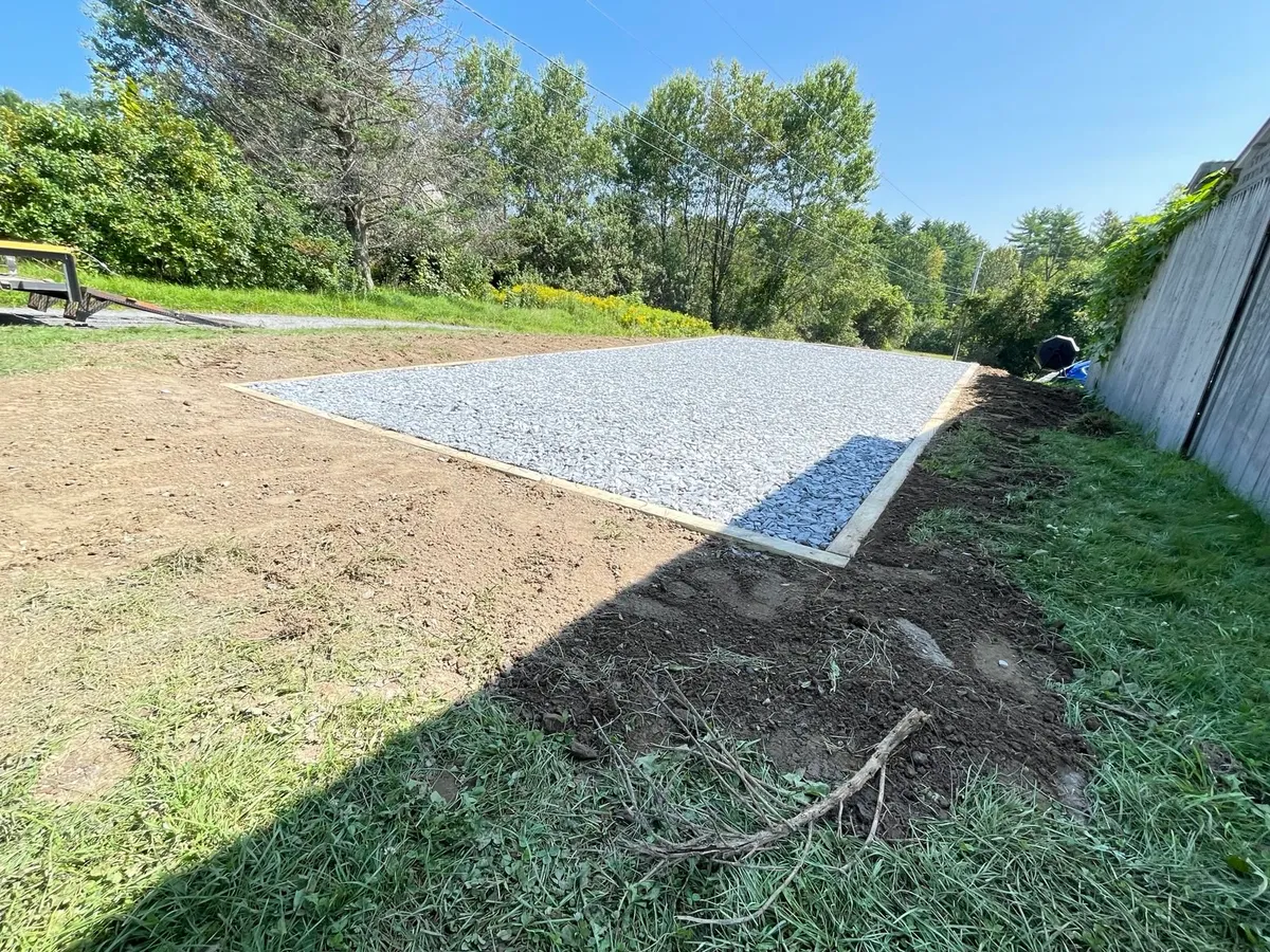Rectangular crushed-stone pad with timber edging beside a building.